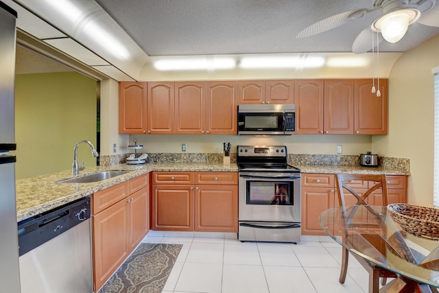 kitchen featuring ceiling fan, sink, stainless steel appliances, light stone counters, and a textured ceiling