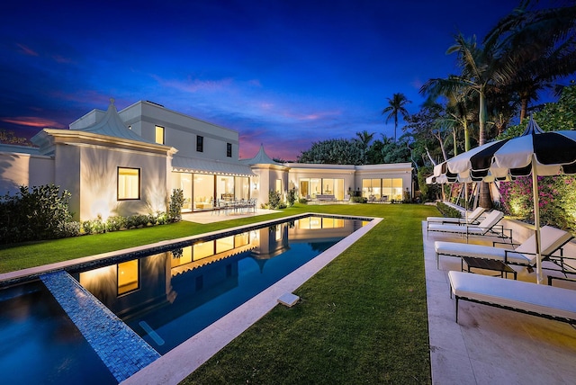 pool at dusk with a patio area and a lawn