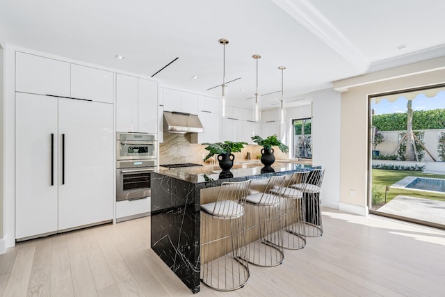 kitchen with double oven, wall chimney range hood, light hardwood / wood-style flooring, paneled refrigerator, and a center island