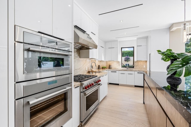 kitchen with pendant lighting, appliances with stainless steel finishes, white cabinetry, decorative backsplash, and dark stone counters