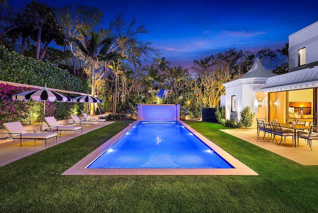 pool at dusk with a patio area and a lawn