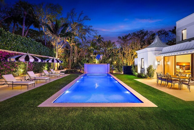 pool at dusk featuring a patio and a lawn