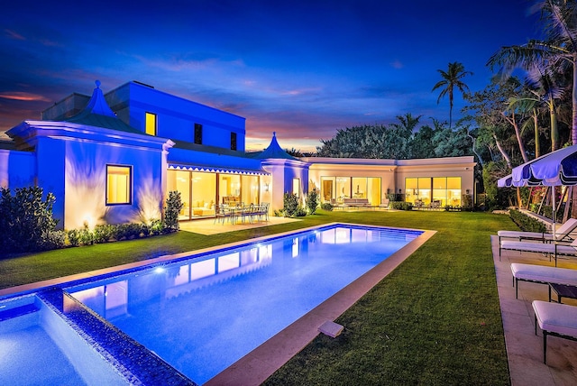 pool at dusk featuring a patio and a lawn