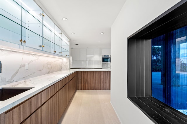 bar featuring sink, white cabinetry, tasteful backsplash, light hardwood / wood-style flooring, and oven