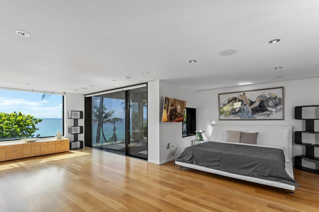 bedroom with a water view, a wall of windows, wood-type flooring, and access to exterior