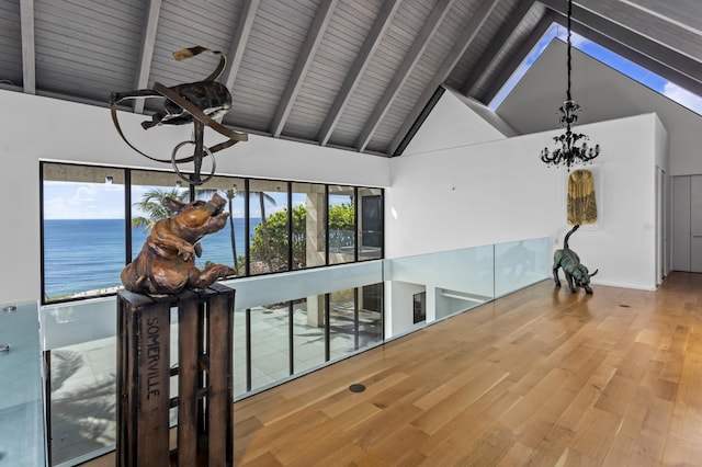 interior space with an inviting chandelier, high vaulted ceiling, wood-type flooring, a water view, and beam ceiling