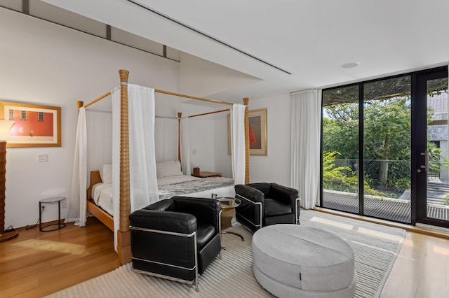 bedroom with access to outside, hardwood / wood-style floors, and a wall of windows