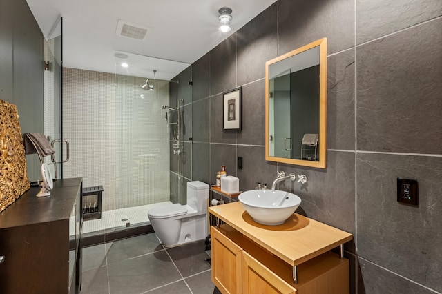 bathroom with tile walls, vanity, toilet, a shower with door, and tile patterned floors