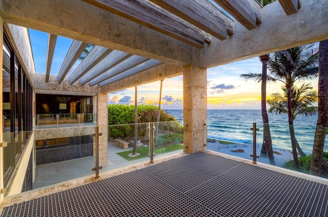 patio terrace at dusk with a water view and a view of the beach