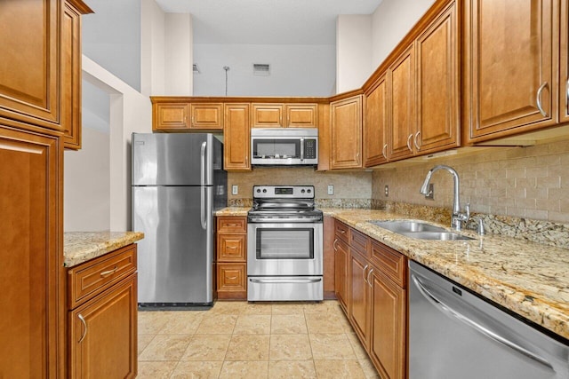 kitchen with sink, stainless steel appliances, light stone counters, backsplash, and light tile patterned floors