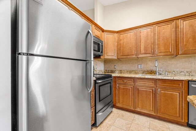 kitchen featuring light stone countertops, appliances with stainless steel finishes, backsplash, sink, and light tile patterned floors