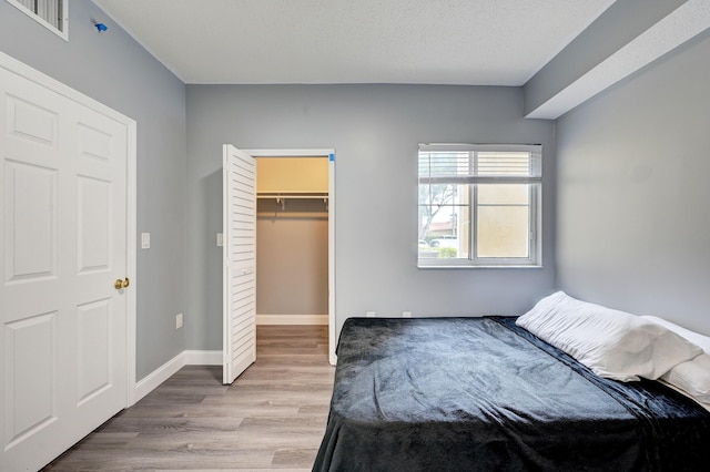 unfurnished bedroom featuring a walk in closet, a closet, light hardwood / wood-style flooring, and a textured ceiling