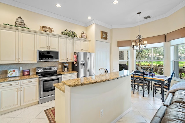 kitchen featuring appliances with stainless steel finishes, a center island, light stone counters, decorative light fixtures, and cream cabinetry