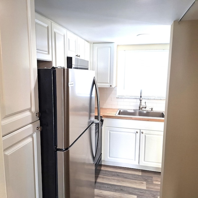 kitchen featuring white cabinets, sink, stainless steel fridge, light wood-type flooring, and tasteful backsplash