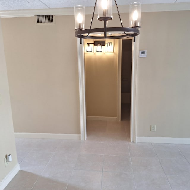 tiled spare room with ornamental molding and an inviting chandelier