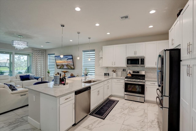 kitchen with light stone countertops, sink, hanging light fixtures, stainless steel appliances, and white cabinets