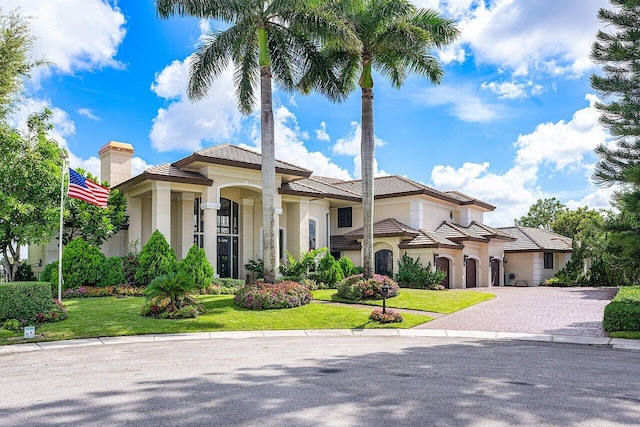 mediterranean / spanish home featuring stucco siding, a chimney, decorative driveway, and a front yard