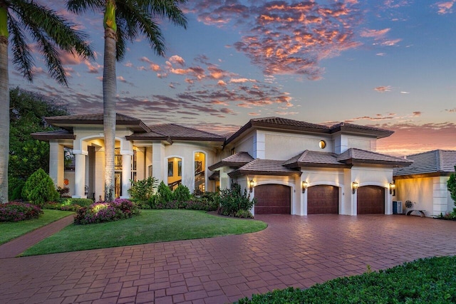 mediterranean / spanish house with an attached garage, decorative driveway, a yard, central air condition unit, and stucco siding