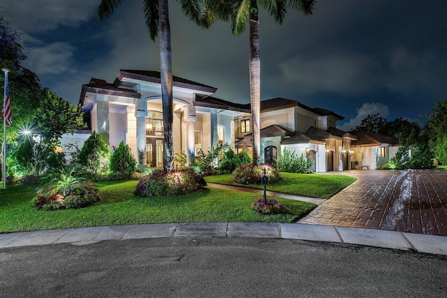 mediterranean / spanish house featuring a garage, decorative driveway, a yard, and stucco siding