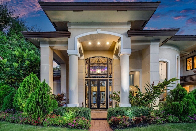 exterior entry at dusk featuring stucco siding and french doors