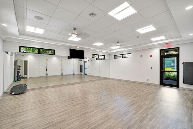 exercise area featuring a tray ceiling, visible vents, light wood-style flooring, a ceiling fan, and baseboards