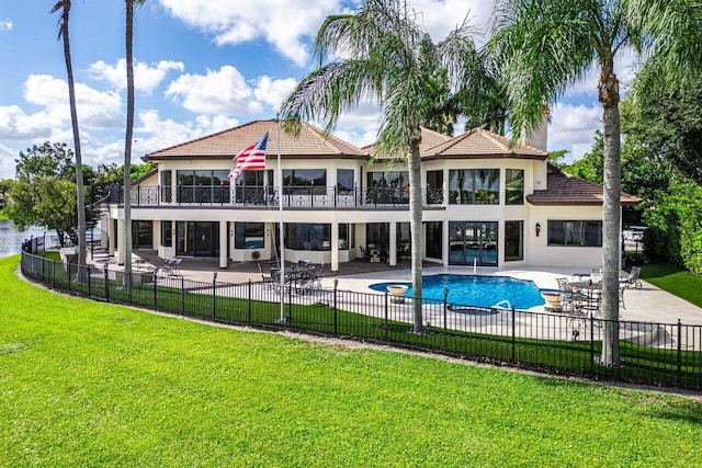 rear view of property featuring a yard, a patio area, fence, and a balcony