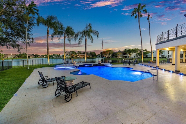 pool at dusk featuring a patio, a yard, fence, and a pool with connected hot tub