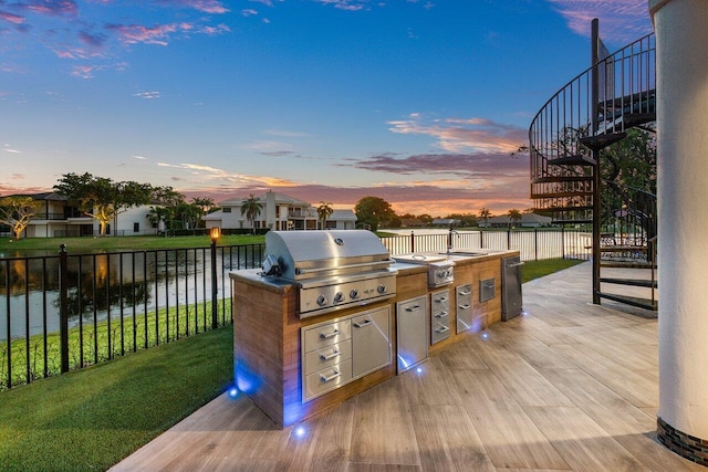 view of patio / terrace featuring a water view, a grill, fence, exterior kitchen, and stairs