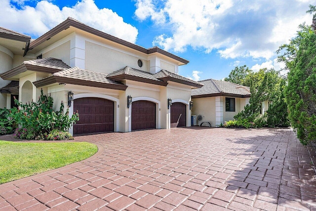 mediterranean / spanish home with a garage, a tiled roof, decorative driveway, and stucco siding