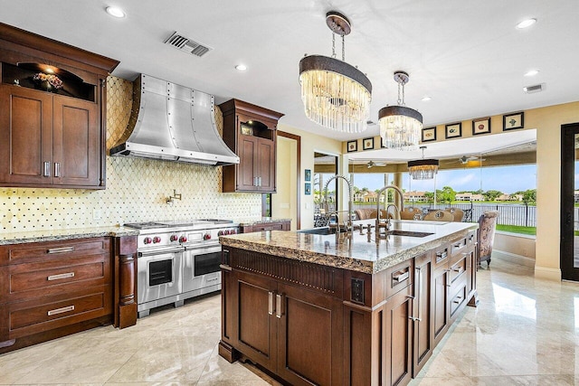 kitchen featuring visible vents, wall chimney exhaust hood, an inviting chandelier, double oven range, and a sink