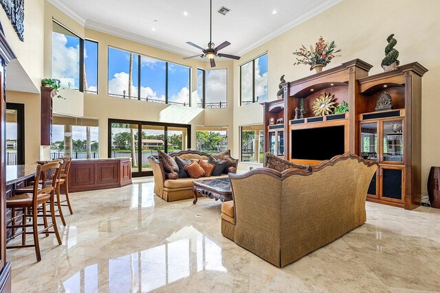 living room featuring a towering ceiling, crown molding, light tile patterned floors, and ceiling fan