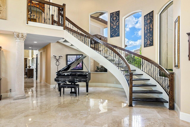 staircase featuring baseboards, marble finish floor, a high ceiling, and ornate columns