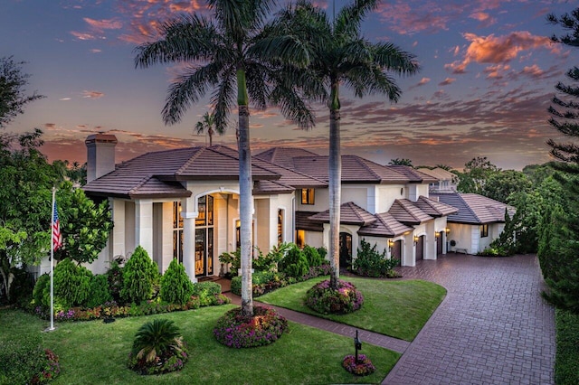 view of front of home featuring a garage, a chimney, decorative driveway, a front yard, and stucco siding