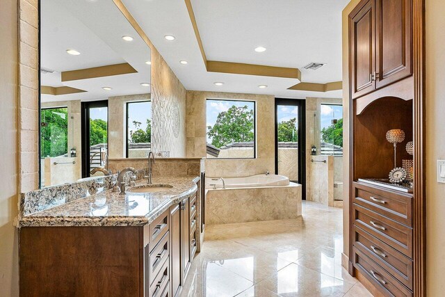 bathroom featuring vanity, tiled tub, a tray ceiling, and a wealth of natural light