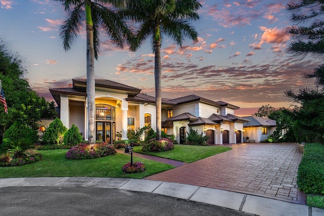 mediterranean / spanish house featuring decorative driveway, a lawn, an attached garage, and stucco siding