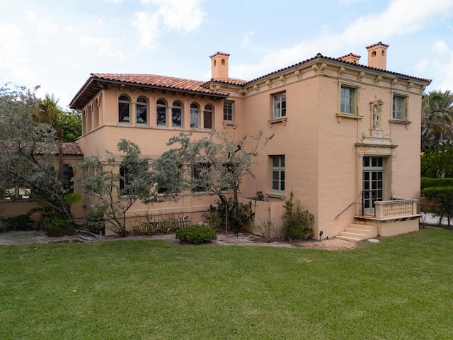 rear view of property with a yard, a chimney, a tiled roof, and stucco siding