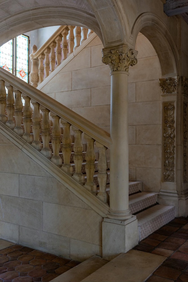 stairway featuring brick floor and ornate columns