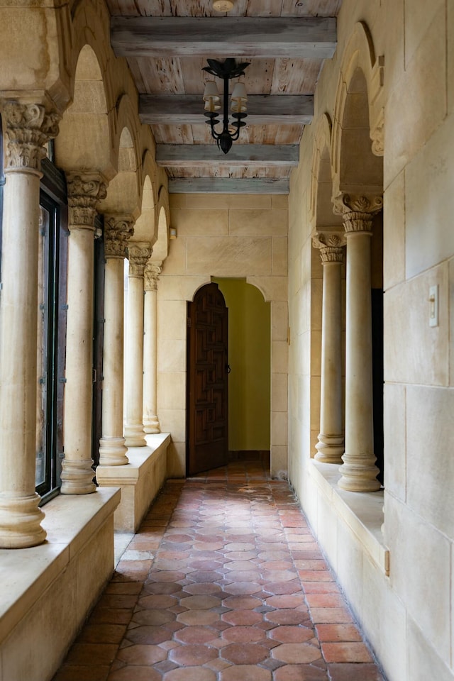 corridor featuring light tile patterned floors, decorative columns, arched walkways, and beam ceiling