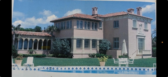 back of property featuring stucco siding, a chimney, and a tiled roof