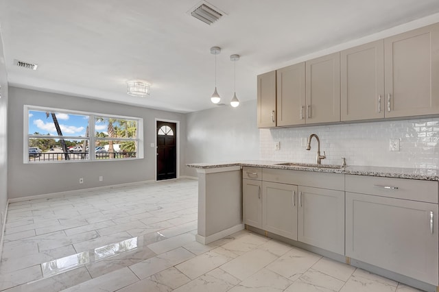 kitchen with hanging light fixtures, sink, light stone counters, and decorative backsplash