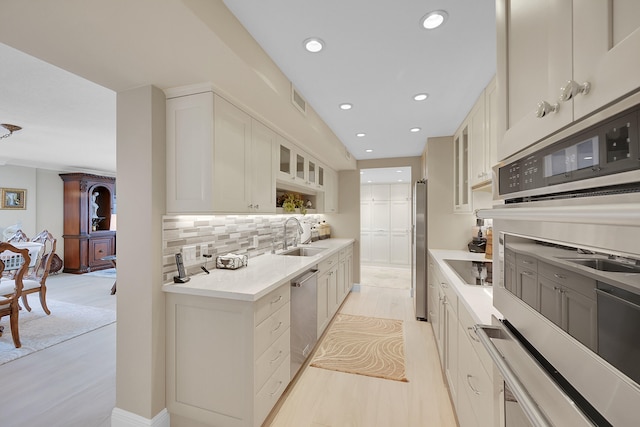 kitchen featuring white cabinetry, sink, stainless steel appliances, tasteful backsplash, and light wood-type flooring