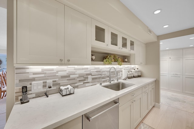 kitchen featuring light stone countertops, light wood-type flooring, tasteful backsplash, stainless steel dishwasher, and sink