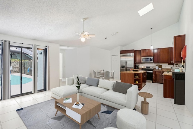 living room featuring ceiling fan, vaulted ceiling with skylight, light tile patterned floors, and a textured ceiling