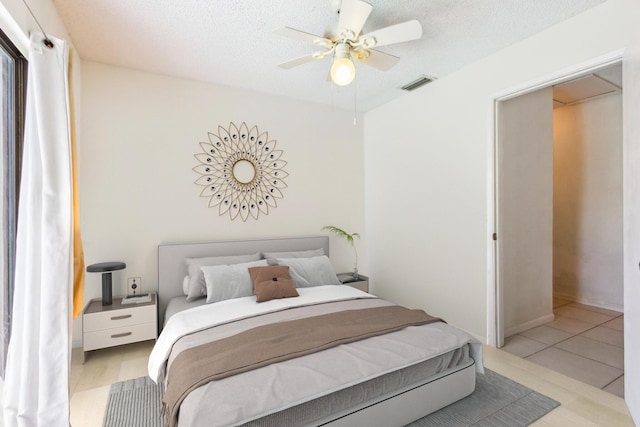 bedroom featuring ceiling fan, light tile patterned floors, and a textured ceiling