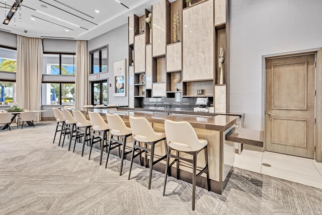 kitchen featuring light tile patterned floors, kitchen peninsula, a high ceiling, and a kitchen breakfast bar