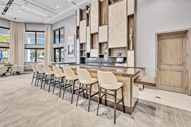 kitchen with a towering ceiling, modern cabinets, a kitchen island, a breakfast bar, and open shelves