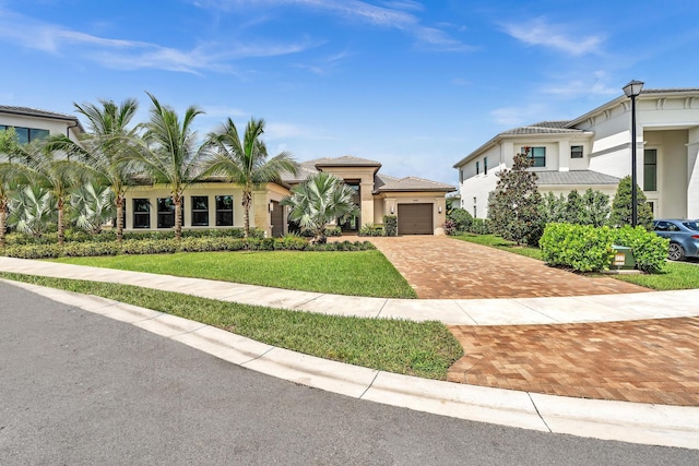 view of front of home with an attached garage, a tiled roof, decorative driveway, stucco siding, and a front yard