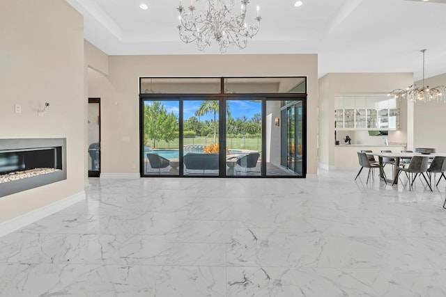 unfurnished living room featuring a chandelier, recessed lighting, baseboards, marble finish floor, and a tray ceiling