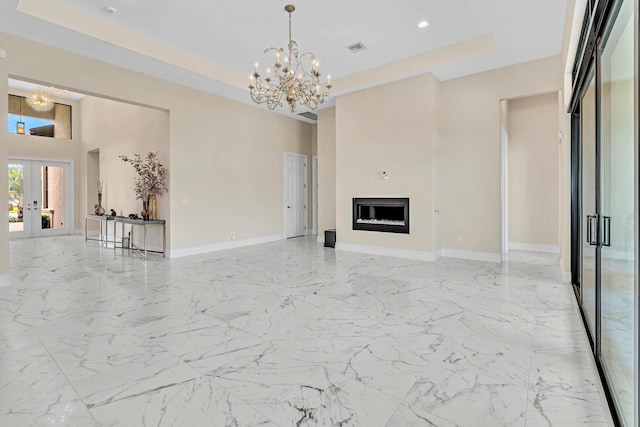 unfurnished living room featuring light tile patterned floors, an inviting chandelier, french doors, a tray ceiling, and a towering ceiling