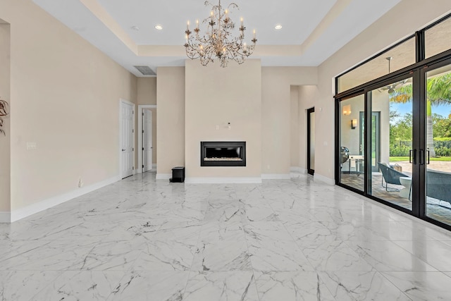 unfurnished living room featuring french doors, a tray ceiling, a glass covered fireplace, and baseboards